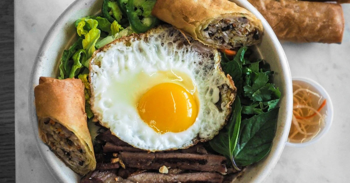Egg Dishes for Dinner – sunny-side-up egg with fresh greens, grilled meat, and crispy spring rolls in a bowl.