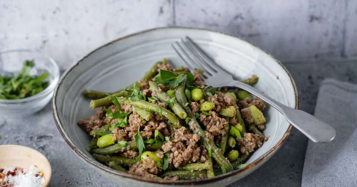 A serving of green beans and ground beef in a bowl, with a fork, highlighting a healthy ground beef meal.