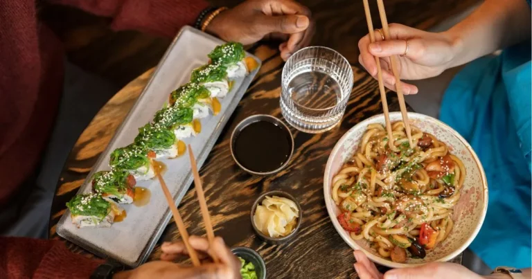 A lively Asian dinner scene with a group of people savoring sushi and noodles together.